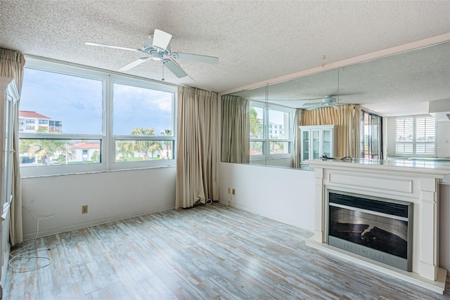 unfurnished living room featuring ceiling fan, plenty of natural light, light hardwood / wood-style floors, and a textured ceiling