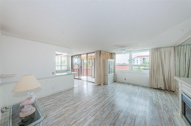 unfurnished living room featuring ceiling fan, light hardwood / wood-style floors, and a textured ceiling