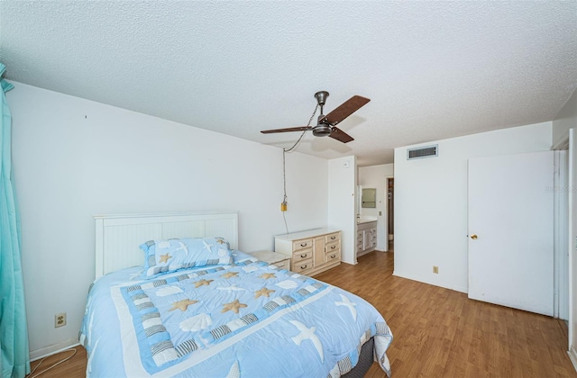 bedroom with a textured ceiling, light hardwood / wood-style floors, ceiling fan, and connected bathroom