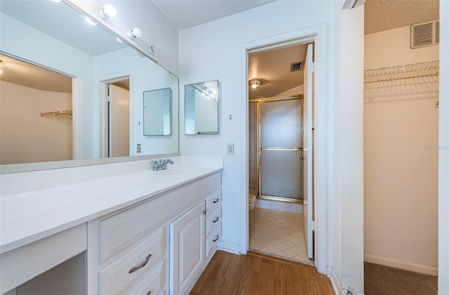 bathroom featuring hardwood / wood-style flooring, vanity, a shower with shower door, and a textured ceiling