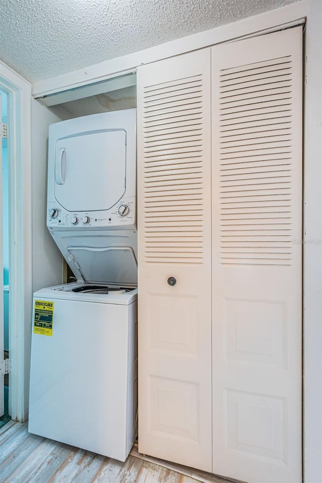 laundry area with a textured ceiling, light hardwood / wood-style flooring, and stacked washer / drying machine