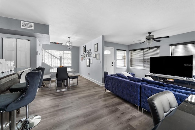 living room with a healthy amount of sunlight, dark wood-type flooring, ceiling fan with notable chandelier, and a textured ceiling