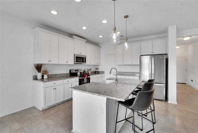 kitchen featuring white cabinetry, sink, light stone counters, an island with sink, and appliances with stainless steel finishes