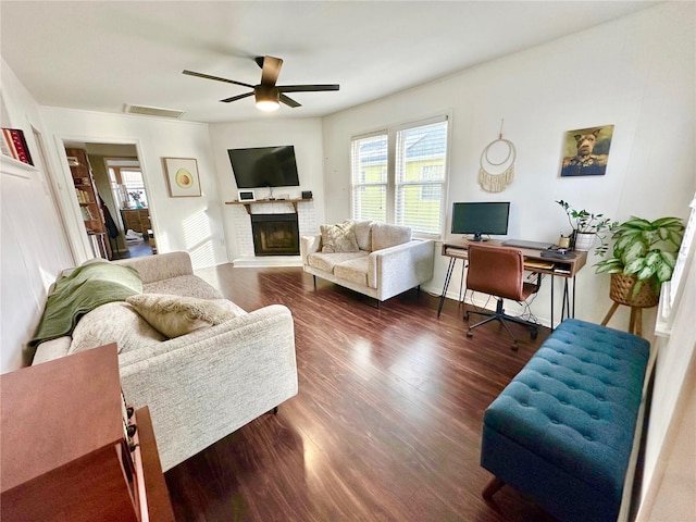 living room featuring dark hardwood / wood-style flooring, a brick fireplace, and ceiling fan