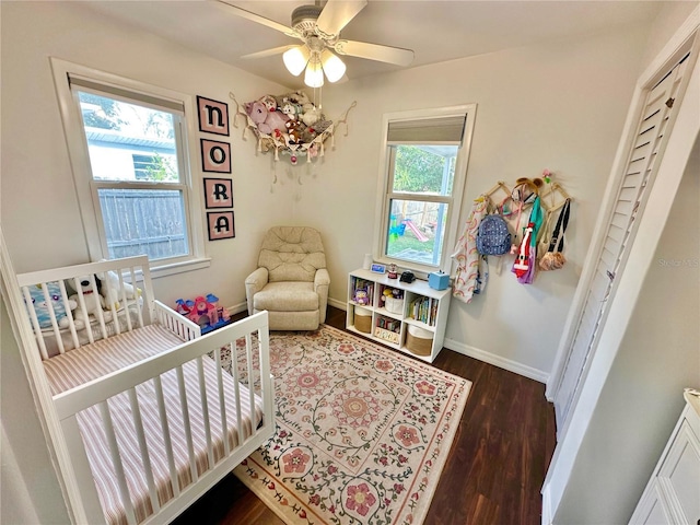 bedroom with multiple windows, dark hardwood / wood-style flooring, a nursery area, and ceiling fan