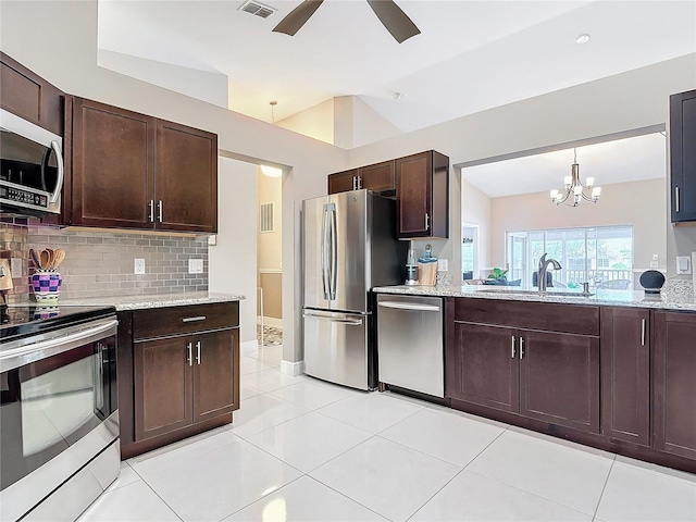 kitchen with decorative backsplash, light stone counters, dark brown cabinets, stainless steel appliances, and vaulted ceiling