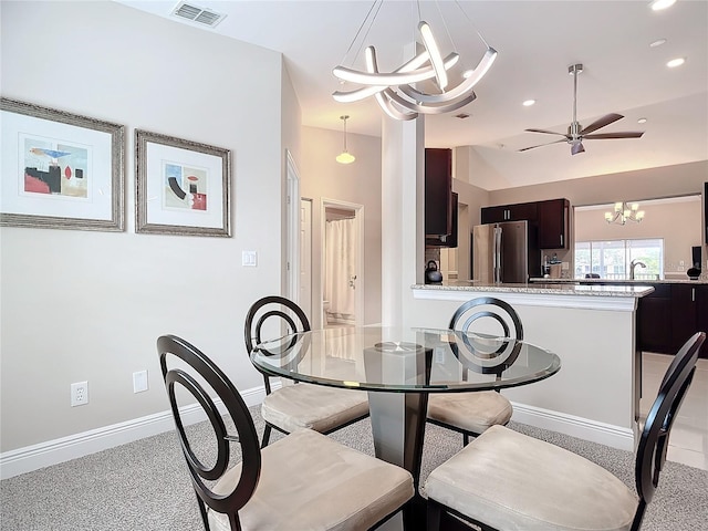 dining area featuring ceiling fan with notable chandelier and sink