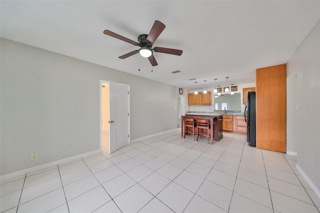 kitchen featuring ceiling fan, a breakfast bar, hanging light fixtures, black refrigerator, and light tile patterned floors