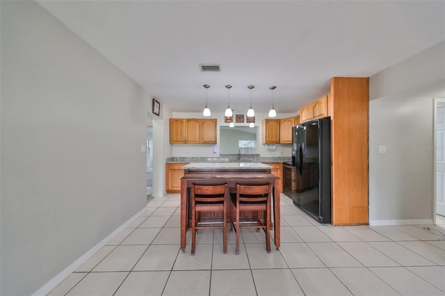 kitchen with decorative light fixtures, a kitchen island, black fridge, a breakfast bar, and light tile patterned floors