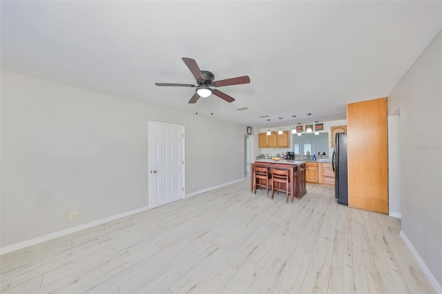 living area with a ceiling fan, light wood-style flooring, and baseboards