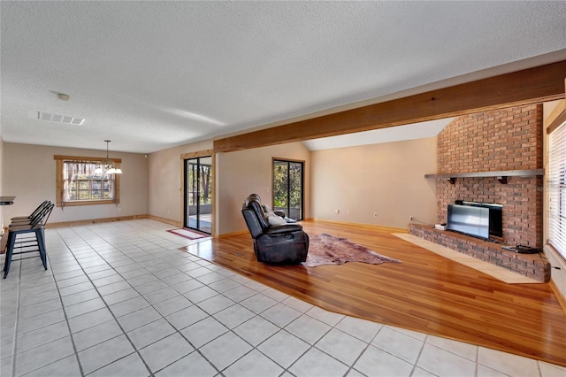 unfurnished living room with vaulted ceiling, a brick fireplace, a textured ceiling, a notable chandelier, and light tile patterned flooring