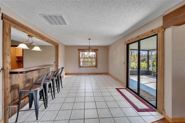 unfurnished dining area featuring a chandelier, light tile patterned floors, a textured ceiling, and bar