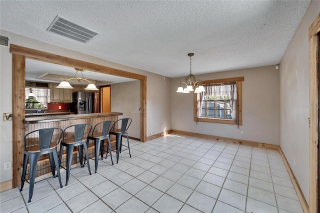 kitchen with an inviting chandelier, stainless steel fridge, light tile patterned floors, a kitchen bar, and kitchen peninsula