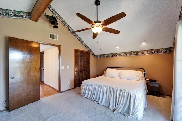 carpeted bedroom with ceiling fan, lofted ceiling with beams, a textured ceiling, and a closet