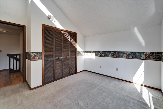 additional living space with a textured ceiling, lofted ceiling, and light carpet