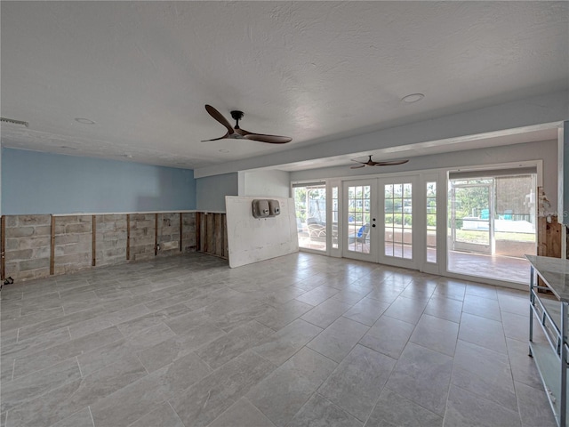 unfurnished living room featuring a textured ceiling, ceiling fan, french doors, and plenty of natural light