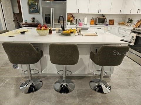 kitchen with appliances with stainless steel finishes, backsplash, a kitchen breakfast bar, and an island with sink