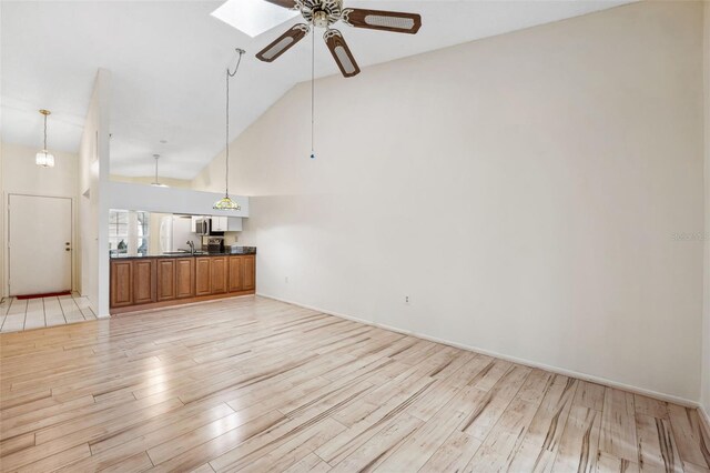 unfurnished living room featuring a skylight, ceiling fan, high vaulted ceiling, and light wood-type flooring