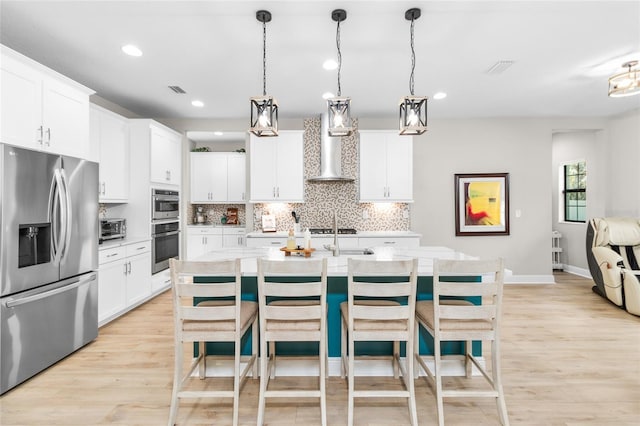 kitchen featuring wall chimney exhaust hood, a kitchen island with sink, appliances with stainless steel finishes, and pendant lighting