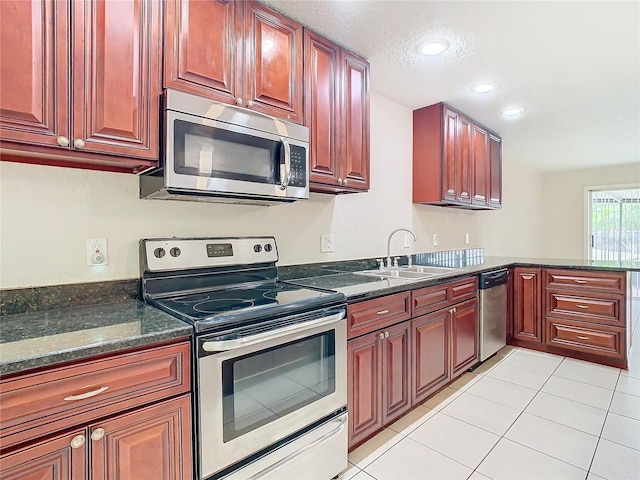 kitchen featuring sink, light tile patterned floors, stainless steel appliances, and dark stone counters