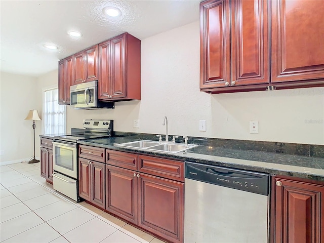 kitchen with light tile patterned flooring, appliances with stainless steel finishes, dark stone countertops, and sink