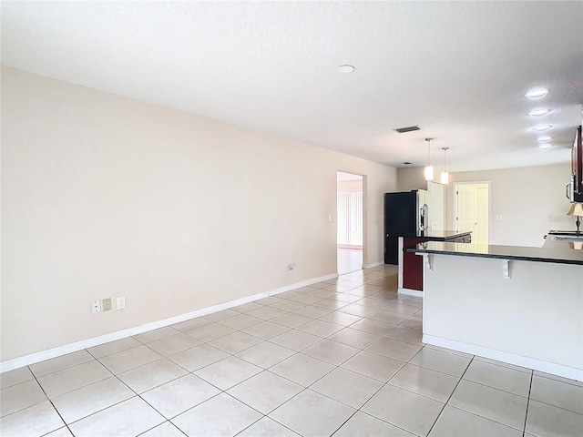 kitchen featuring a kitchen bar, light tile patterned floors, decorative light fixtures, and stainless steel fridge