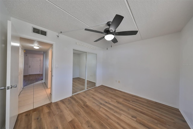 unfurnished bedroom featuring ceiling fan, a closet, hardwood / wood-style floors, and a textured ceiling