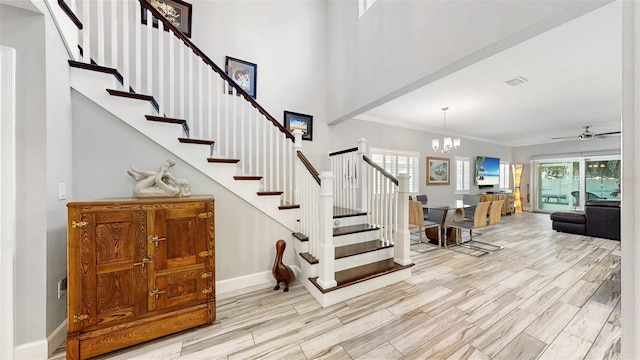 stairway with wood-type flooring, ceiling fan with notable chandelier, and crown molding