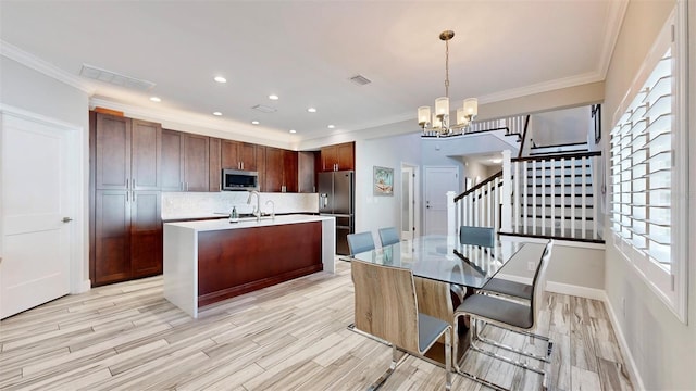 kitchen featuring appliances with stainless steel finishes, light hardwood / wood-style flooring, an inviting chandelier, hanging light fixtures, and an island with sink