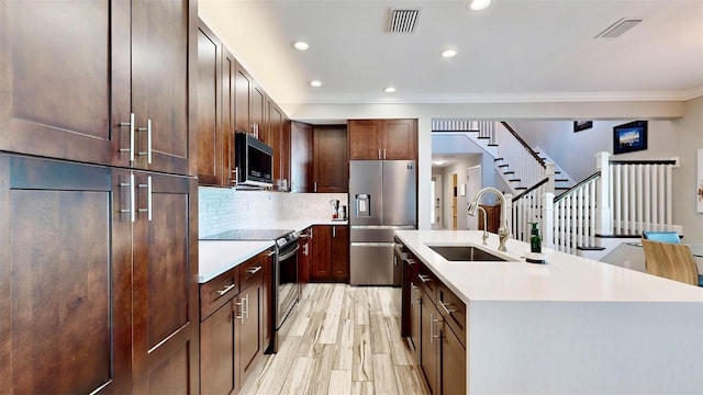 kitchen featuring appliances with stainless steel finishes, tasteful backsplash, ornamental molding, a kitchen island with sink, and sink