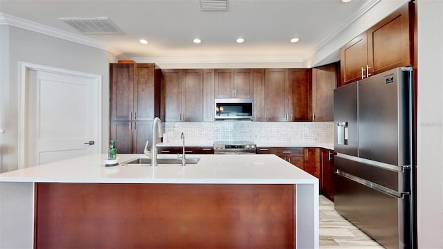 kitchen featuring decorative backsplash, appliances with stainless steel finishes, a kitchen island with sink, crown molding, and sink