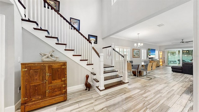 stairway featuring a towering ceiling, ceiling fan with notable chandelier, crown molding, and wood-type flooring