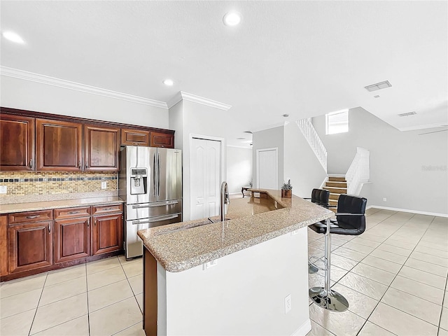 kitchen featuring a kitchen breakfast bar, stainless steel refrigerator with ice dispenser, crown molding, a center island with sink, and light tile patterned floors