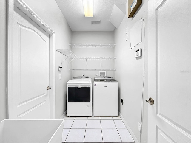 clothes washing area with light tile patterned floors, a textured ceiling, and washing machine and clothes dryer