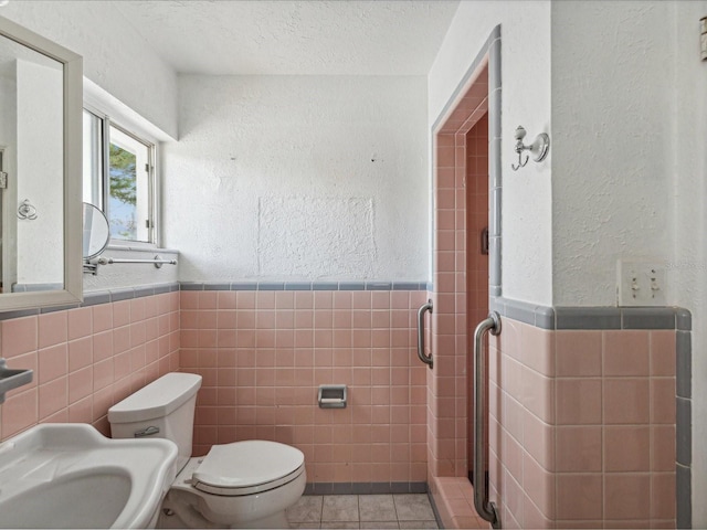 bathroom featuring tile patterned flooring, a textured ceiling, toilet, and tile walls