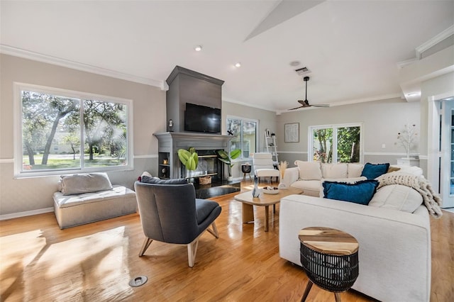 living room featuring ceiling fan, a large fireplace, crown molding, vaulted ceiling, and light wood-type flooring