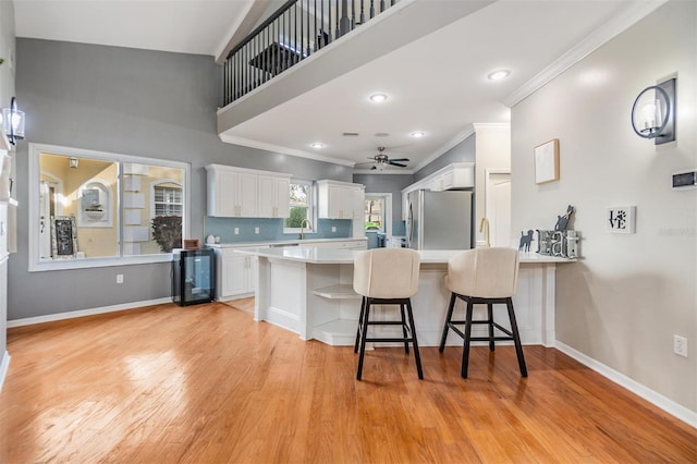 kitchen with kitchen peninsula, stainless steel fridge, light wood-type flooring, a kitchen breakfast bar, and white cabinetry