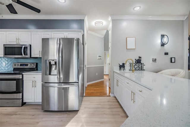 kitchen with light stone countertops, appliances with stainless steel finishes, white cabinetry, and ornamental molding