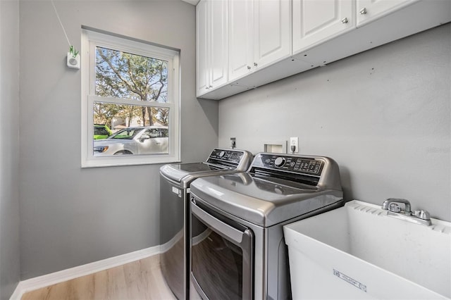 laundry area featuring separate washer and dryer, sink, cabinets, and light hardwood / wood-style floors