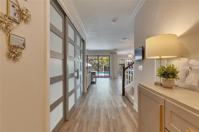 hall with a notable chandelier, light wood-type flooring, ornamental molding, and a textured ceiling