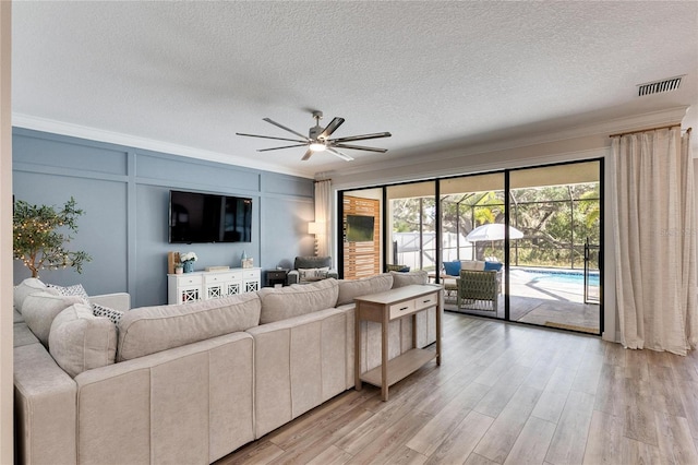 living room with light wood-type flooring, a textured ceiling, ceiling fan, and crown molding