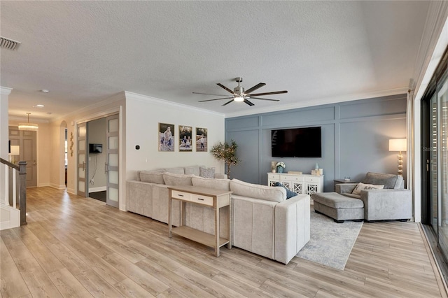 living room with a textured ceiling, light hardwood / wood-style flooring, ceiling fan, and crown molding