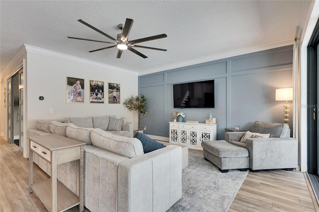 living room with a textured ceiling, ceiling fan, light wood-type flooring, and crown molding