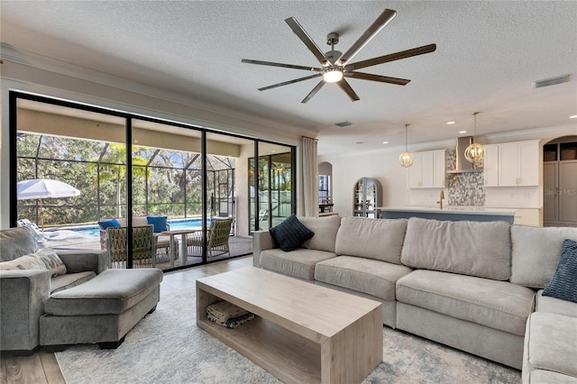 living room featuring ceiling fan, light wood-type flooring, a textured ceiling, and ornamental molding