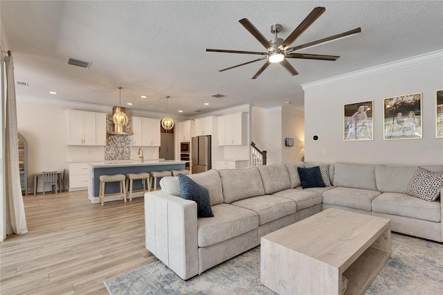 living room featuring ceiling fan, ornamental molding, a textured ceiling, and light hardwood / wood-style flooring