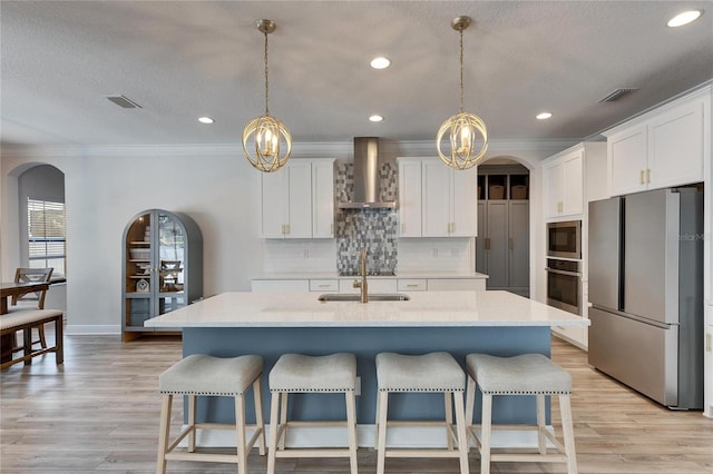 kitchen featuring white cabinets, stainless steel appliances, a kitchen island with sink, and wall chimney exhaust hood