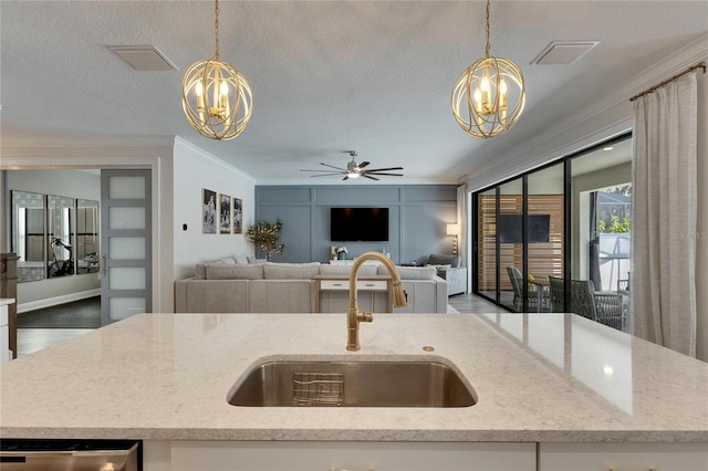 kitchen with a center island with sink, hanging light fixtures, ceiling fan with notable chandelier, and sink