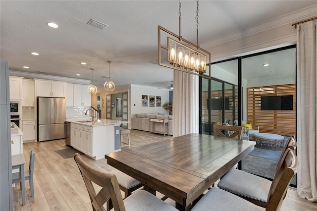 dining space with sink, light hardwood / wood-style floors, a textured ceiling, ceiling fan with notable chandelier, and ornamental molding