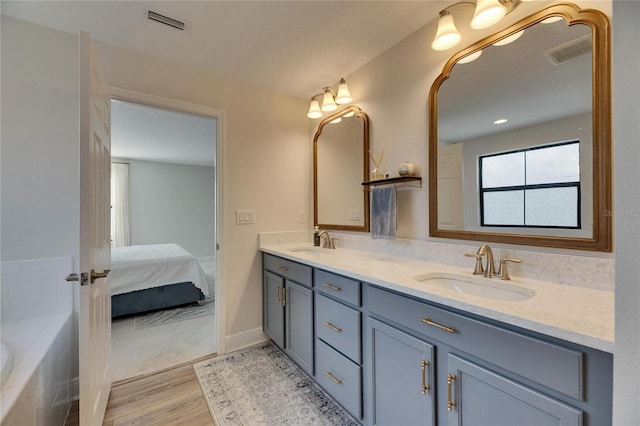 bathroom with hardwood / wood-style floors, vanity, and a relaxing tiled tub