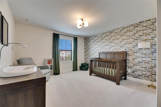 bedroom with light colored carpet, a textured ceiling, and a nursery area